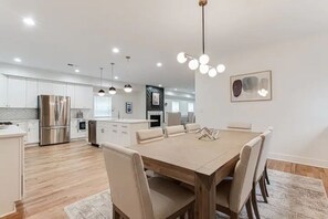 A modern kitchen with stainless steel appliances, a dining area with a wooden table and chairs, and pendant lighting.