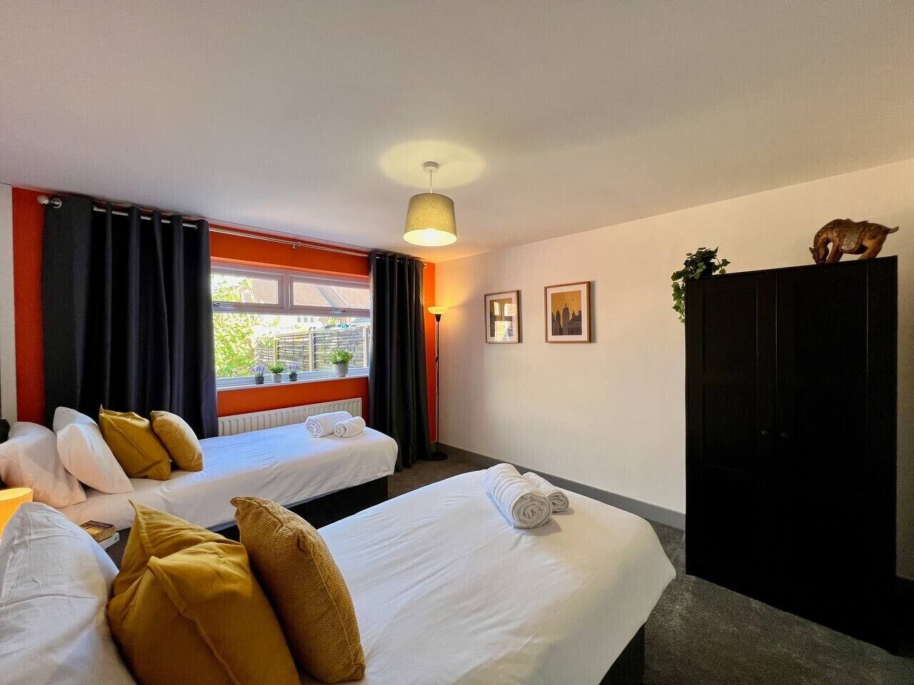 Habitación de hotel con dos camas, una ventana con cortinas, una lámpara y una planta sobre un mueble.