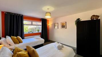 Habitación de hotel con dos camas, una ventana con cortinas, una lámpara y una planta sobre un mueble.