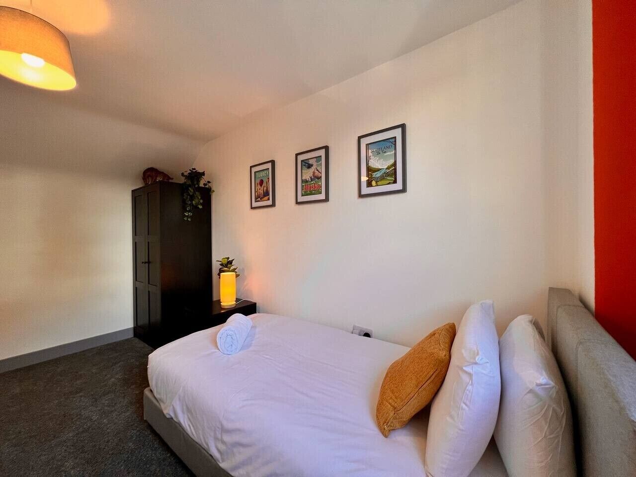 Una habitación de hotel con cama, una mesita de noche con lámpara, un armario y tres cuadros en la pared.