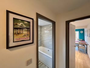 Un couloir orné d’un tableau encadré, une porte vitrée donnant sur une salle de bain, et un aperçu d’un coin repas.
