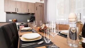 A modern kitchen with wooden cabinets, a coffee machine, and a dining table set for four with wine glasses and plates.