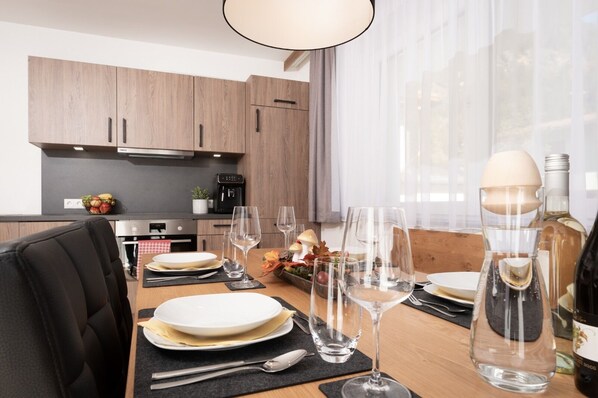 A modern kitchen with wooden cabinets, a coffee machine, and a dining table set for four with wine glasses and plates.