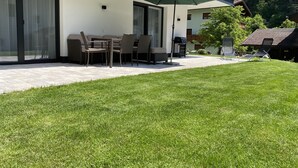 A modern house with a patio, outdoor furniture, and a green umbrella.