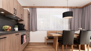 A modern kitchen with wooden cabinets, a dining table with chairs, and a pendant light.