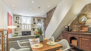 Un comedor con mesa de madera, sillas blancas y pared de ladrillo.