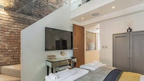 Un dormitorio moderno con una cama grande, un televisor de pantalla plana, una puerta de madera y una pared de ladrillo.