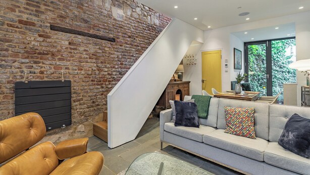 Una sala de estar moderna con una pared de piedra, una escalera, un sofá gris y sillones de cuero.