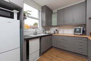 A modern kitchen with grey cabinets, a white refrigerator, a wooden countertop, and a vintage computer monitor.