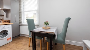 Una cocina compacta con lavadora, una mesa con mantel a rayas y dos sillas de textura trenzada.