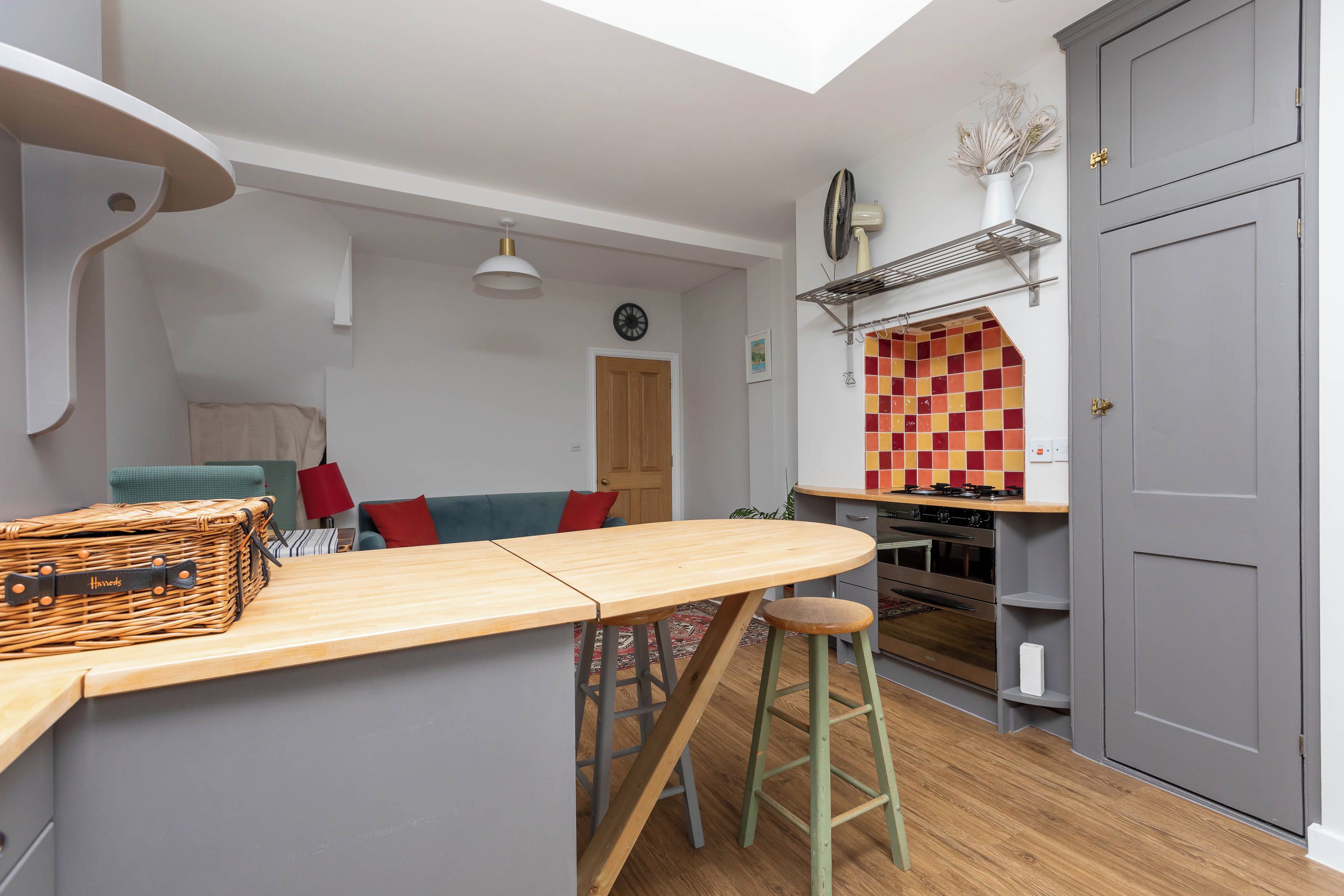 A compact kitchen with a wooden bar, a red and yellow checkered backsplash, a built-in oven, and a grey door.