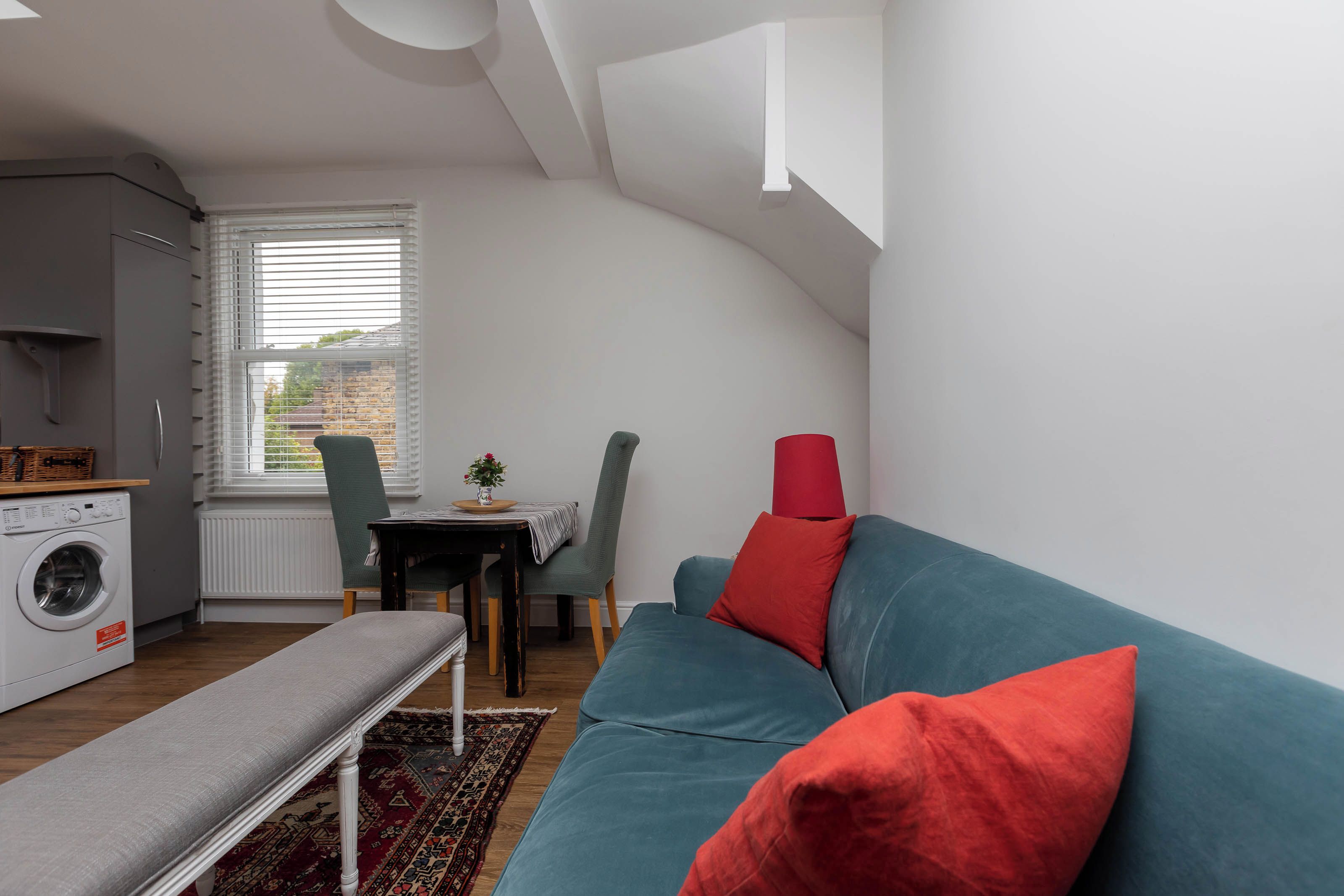 A compact living space with a washing machine, a dining area with a table and chairs, a sofa with cushions, and a bench.