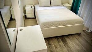 Een moderne hotelkamer met een groot bed, nachtkastje, bijzettafeltje en een klein bureau.