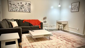 Een moderne woonkamer met een bank, salontafel en vloerkleed. Twee schilderijen hangen aan de muren en op een bijzettafeltje staat een vaas.