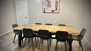 Een rechthoekige houten tafel met zes zwarte stoelen, een witte deur en een abstract kunstwerk in een lijst aan de muur.