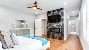 A modern bedroom with a bed, dresser, and a fireplace. - Modern relaxing home w/ movie room & massage chair (Atlanta)