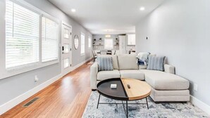 A modern living room with a sectional sofa, a coffee table, and a view of the kitchen in the background. - Modern relaxing home w/ movie room & massage chair (Atlanta)