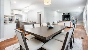 A modern kitchen with white cabinetry, a central island, and a dining area with a large table and chairs. - Modern relaxing home w/ movie room & massage chair (Atlanta)