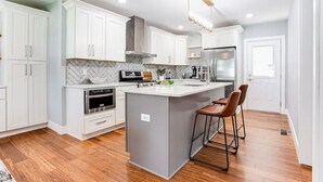 A modern kitchen with white cabinetry, a marble backsplash, a central island with stools, and a stainless steel refrigerator. - Modern relaxing home w/ movie room & massage chair (Atlanta)