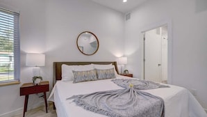 Een slaapkamer met een groot bed, twee nachtkastjes, een ronde spiegel en een deur.