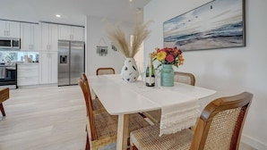 Een moderne keuken met witte kasten, roestvrijstalen apparatuur en een eethoek met een witte tafel en rieten stoelen.