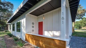Een modern huis met een rode deur, een witte gevel en een houten terras.