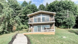 Ein zweigeschossiges Haus mit einem Balkon im oberen Geschoss, einer Veranda mit Sitzgelegenheiten im Freien und einer Treppe zum Eingang.