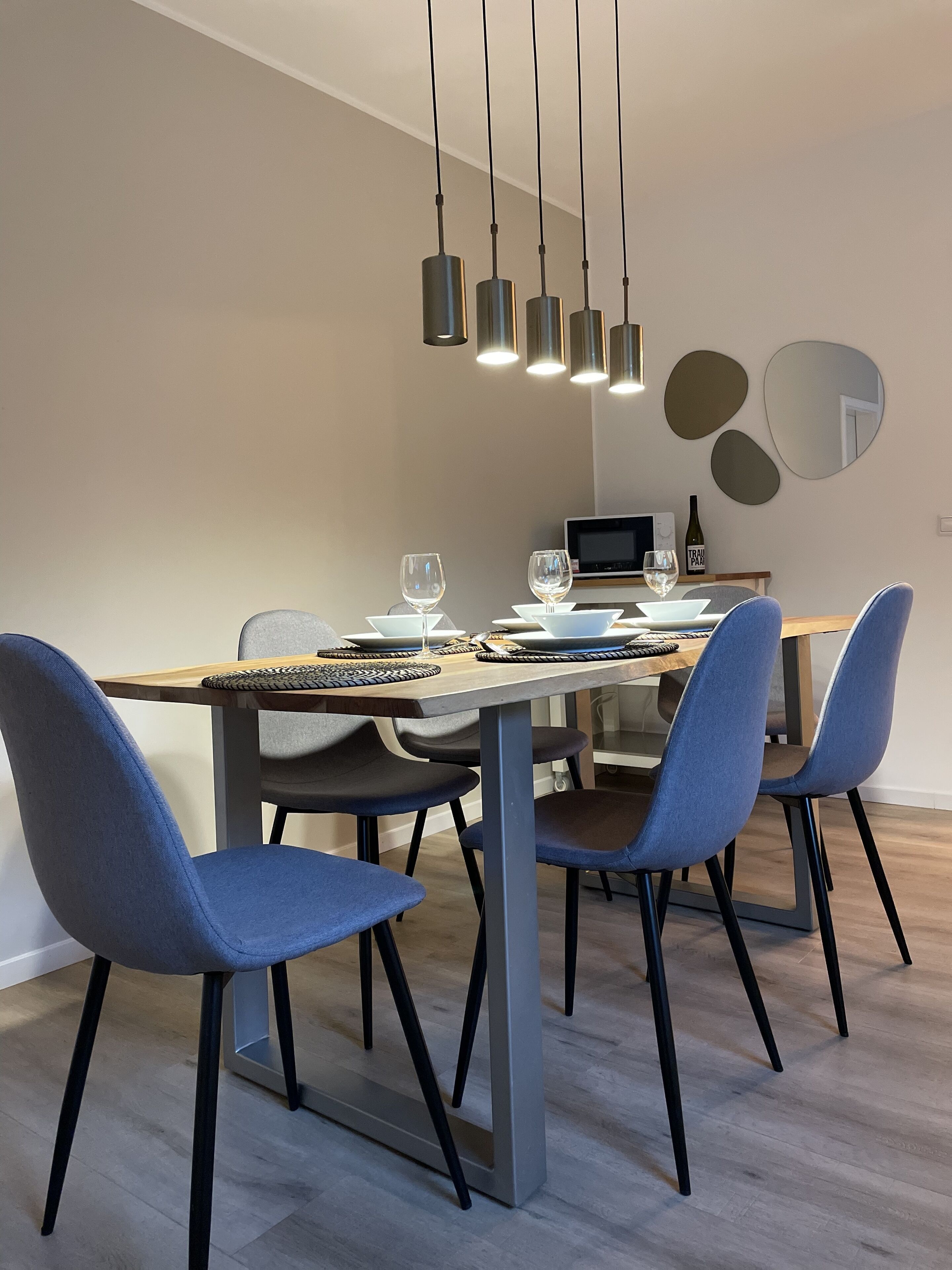 A modern dining area with a rectangular table, four blue chairs, and a pendant light fixture.