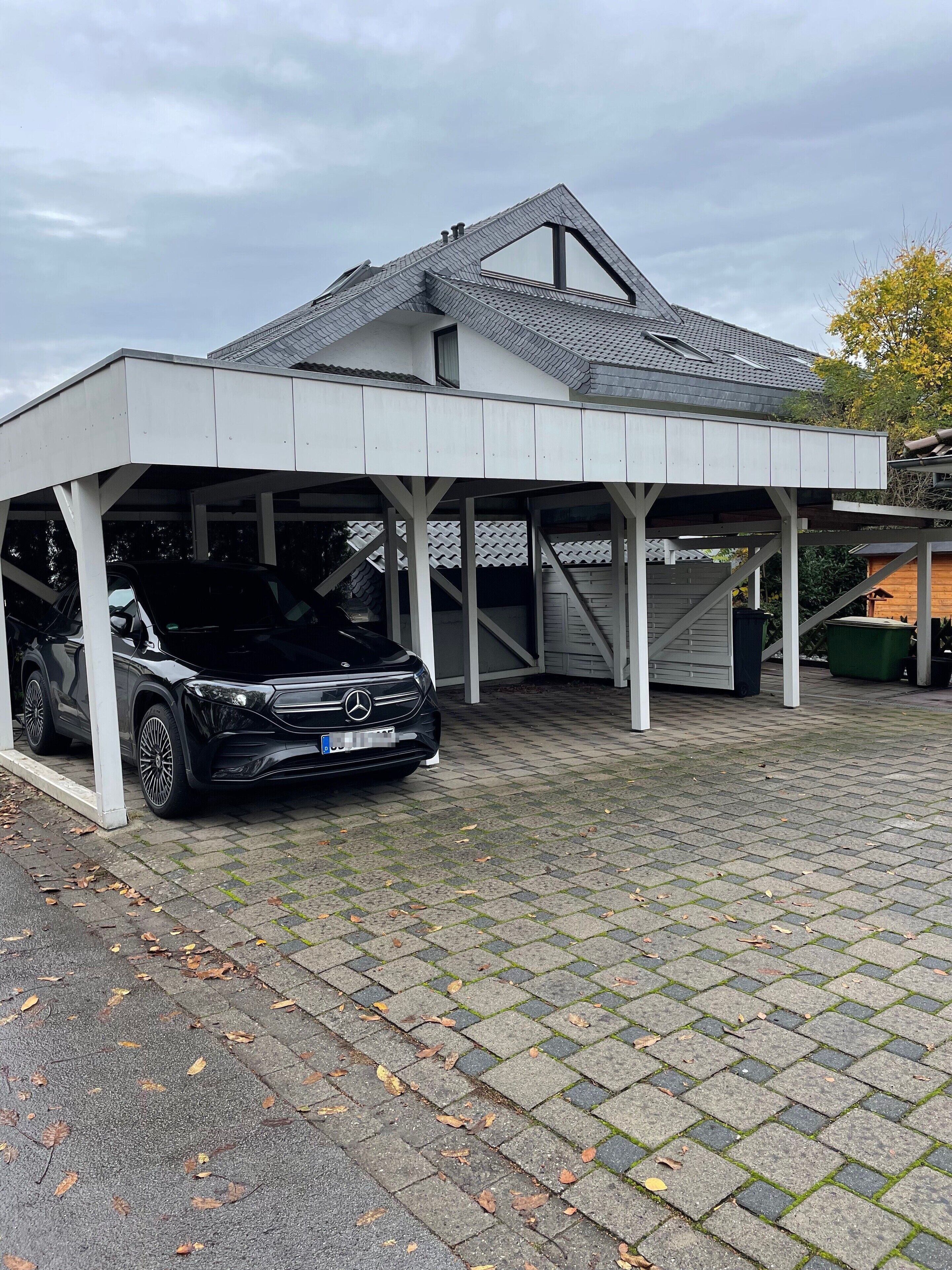 A covered parking area with a black car parked under a white structure.
