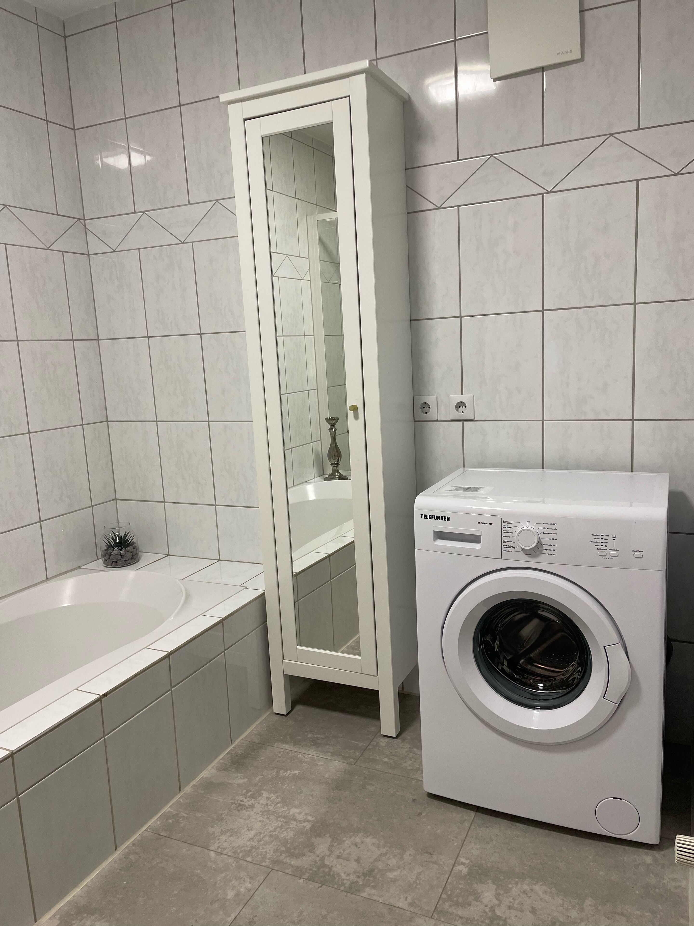 A bathroom with a white washing machine, a mirror cabinet, and a bathtub.