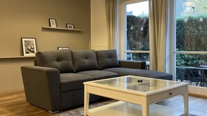 Moderni olohuone, jossa on harmaa sohva, lasinen sohvapöytä ja kattovalaisin.