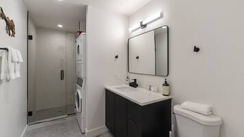 A modern bathroom with a glass shower enclosure, a white toilet, and a black vanity with a mirror.