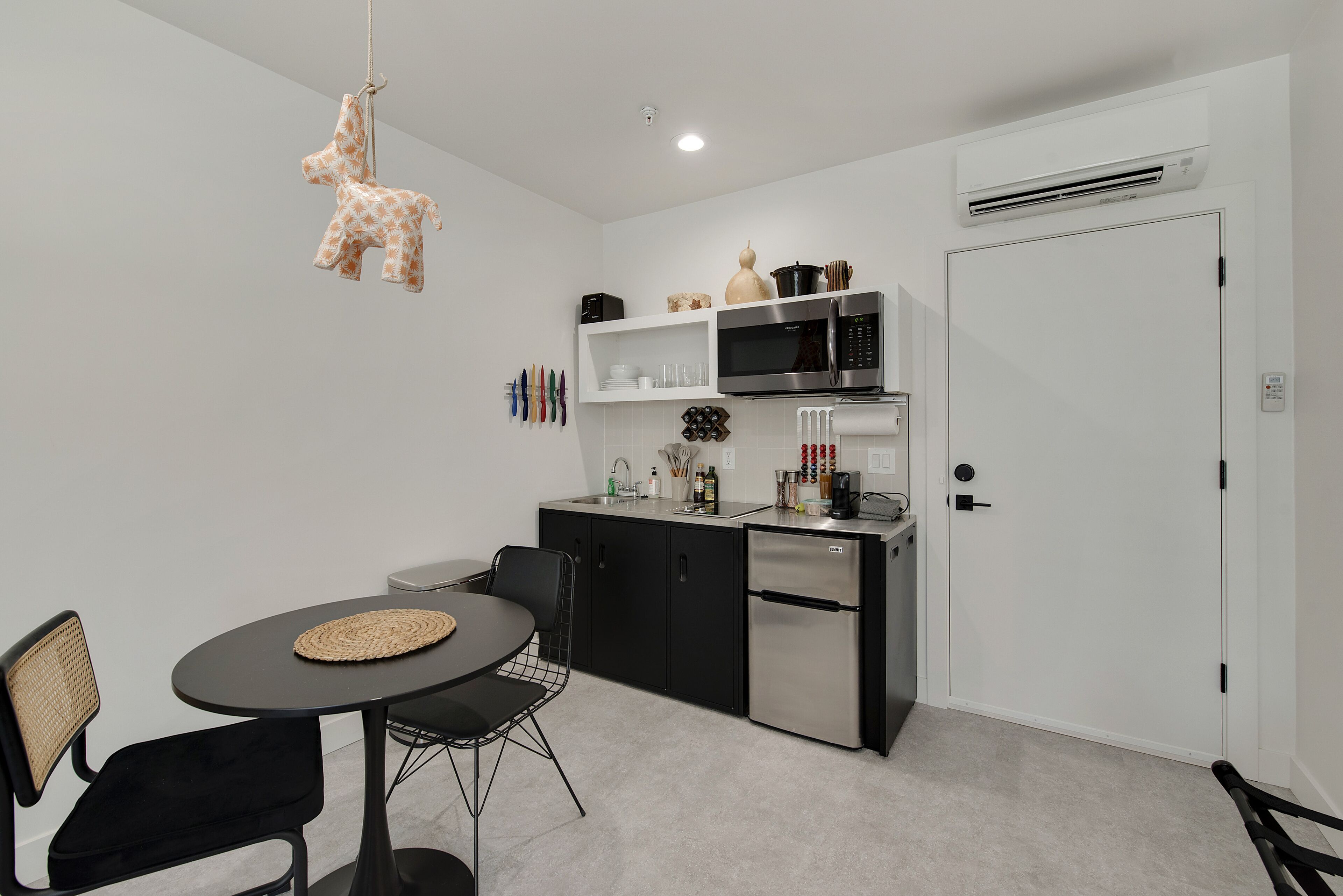 A compact kitchen with modern appliances, a dining area with a round table and chairs, and a hanging giraffe ornament.