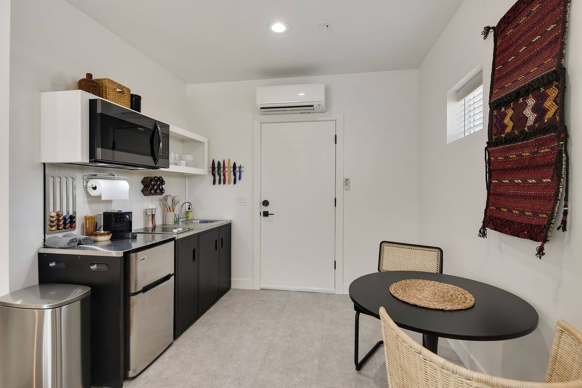 Une cuisine compacte équipée d’un four à micro-ondes, d’une cuisinière et d’un réfrigérateur, un petit coin repas avec une table et des chaises, et une porte avec une fenêtre.