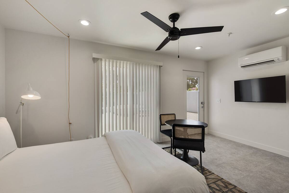 Une chambre d’hôtel moderne équipée d’un lit, d’un bureau, d’une chaise, d’un ventilateur de plafond et d’un téléviseur fixé au mur.
