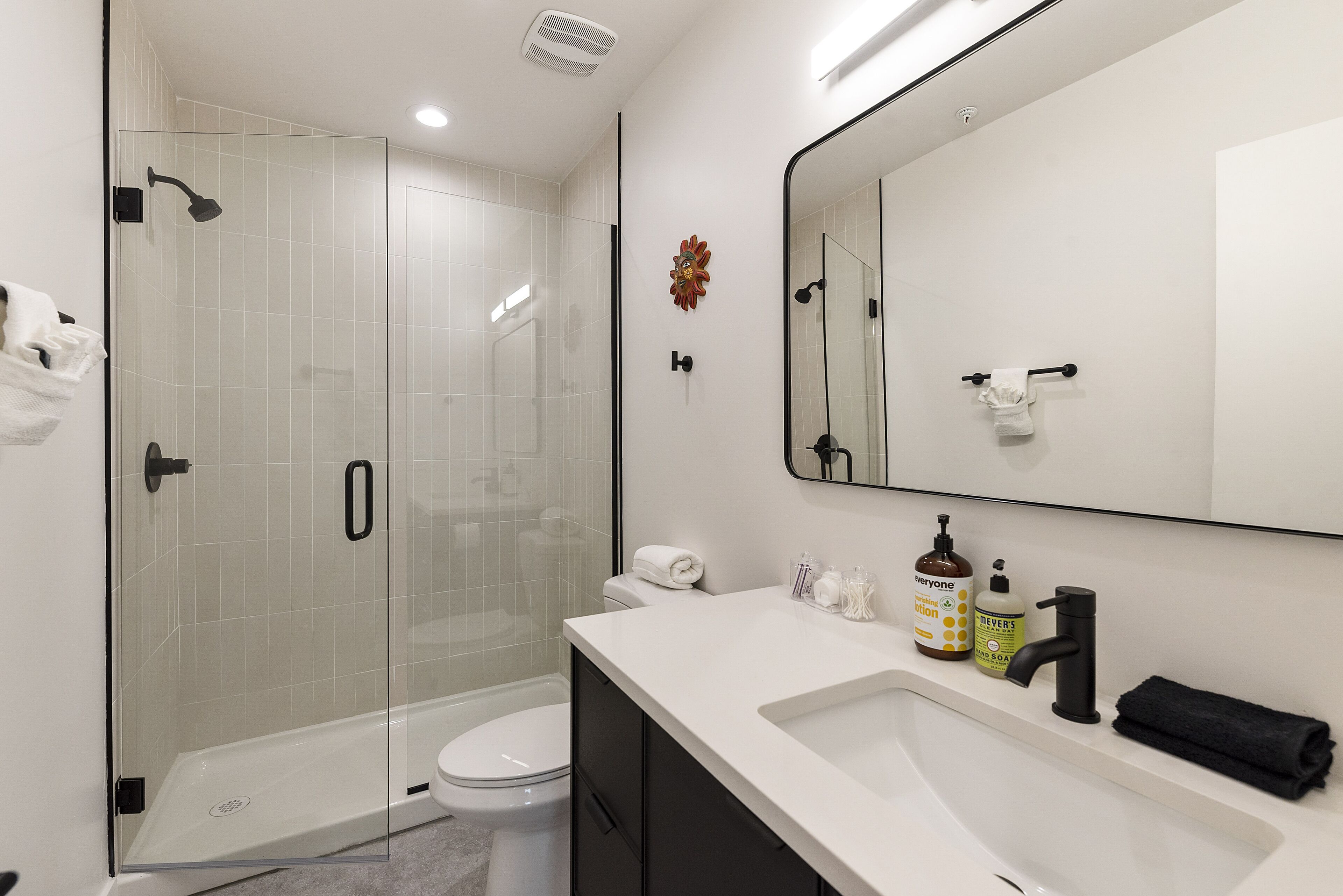 Une salle de bain moderne avec une douche à parois de verre, des toilettes, un lavabo avec des articles de toilette et un grand miroir.