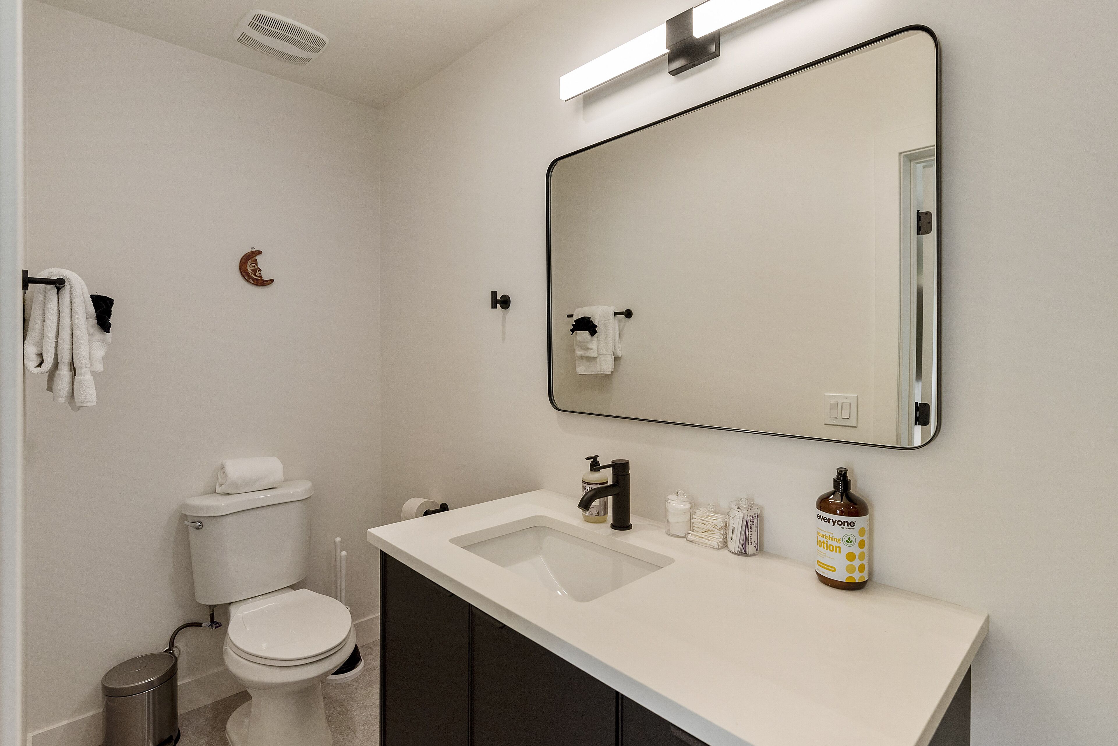 Un baño moderno con un lavabo blanco, grifo negro y un espejo grande encima.