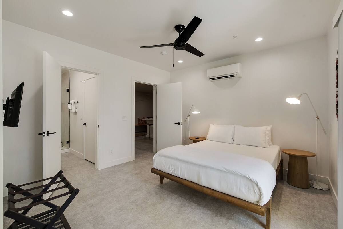 Une chambre à coucher comprenant un lit, un ventilateur de plafond, des spots encastrés, un appareil de climatisation et une table de chevet.