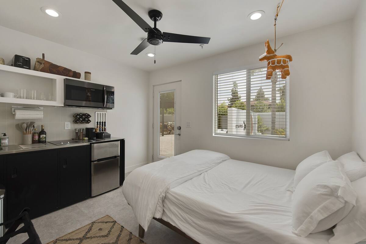 Une chambre à coucher avec un lit, un ventilateur de plafond, une fenêtre avec des stores et une vue sur l’extérieur.