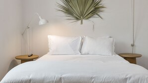 Een netjes ingerichte slaapkamer met een groot bed, nachtkastjes, een hangplant en een rieten kist.