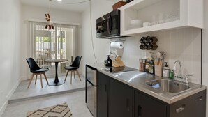 Een moderne keuken met een roestvrijstalen spoelbak, een magnetron en een ingebouwde oven. Er is een eethoek met een ronde tafel en twee stoelen.