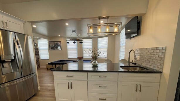 A modern kitchen with a central island, white cabinetry, stainless steel appliances, and a brick backsplash.