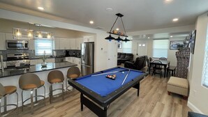 A modern kitchen with stainless steel appliances, a dining area with a pool table, and a cozy seating area.
