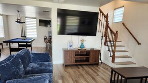 A living room with a blue sofa, a wooden entertainment center, a TV mounted on the wall, and a wooden staircase.