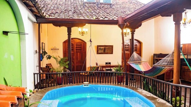 A swimming pool with a wooden deck, a hammock, and a dining area with chairs and a table. - You’ll know that you have rented a historic colonial home when you pass through huge, antique front doors framed by 3 foot-thick adobe walls. Lounge on the shallow, submerged bench seats in the pool or in the hammocks hanging between 12 foot wooden c (Granada)