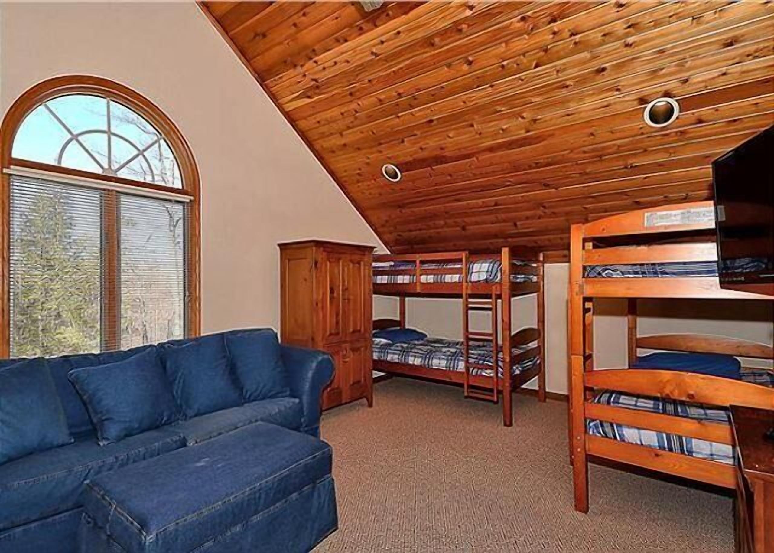 A room with bunk beds, a blue sofa, and a wooden ceiling.