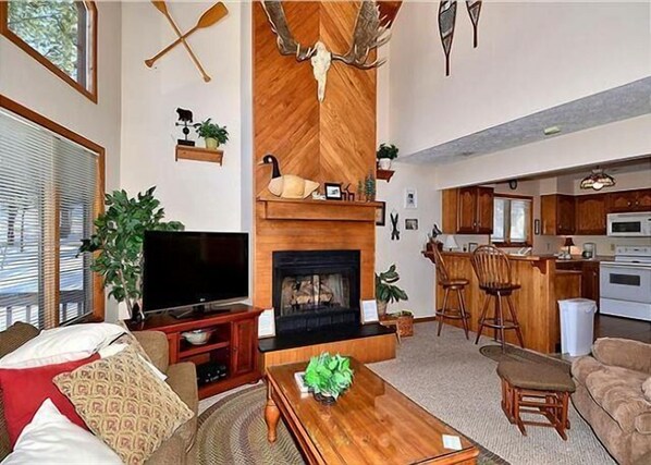 A living room with a fireplace, a television, and a kitchen area with bar stools.