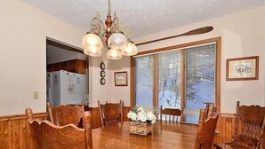 Comedor con mesa de madera, sillas, una lámpara de araña y ventana con persianas.