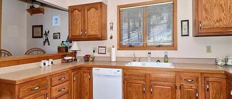 A kitchen with wooden cabinets, a dishwasher, a sink, and a window with blinds.