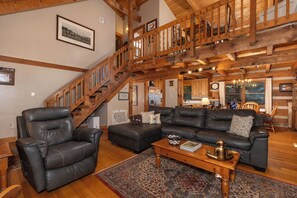 A spacious living room with a high wooden ceiling, a staircase, leather sofas, and a coffee table.